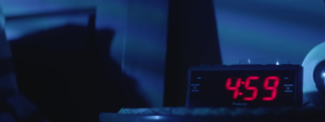An alarm clock goes off  in a dark bedroom
