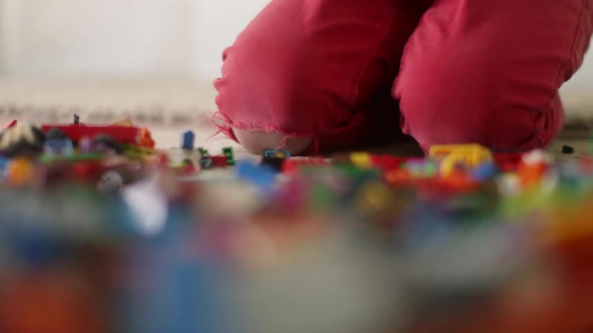 A child is playing in a room with many pieces of building block bricks and toys