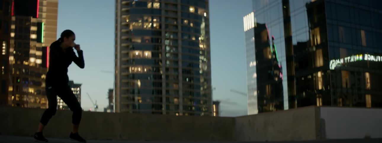 A woman punches the air on a city rooftop at dusk