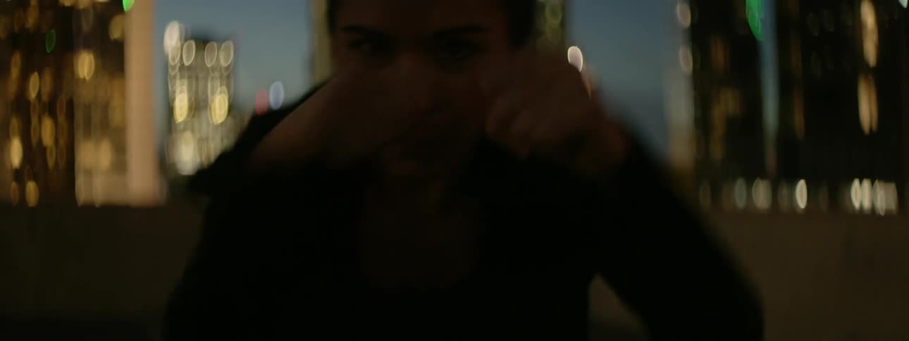 A woman shadow boxes on a city rooftop at night
