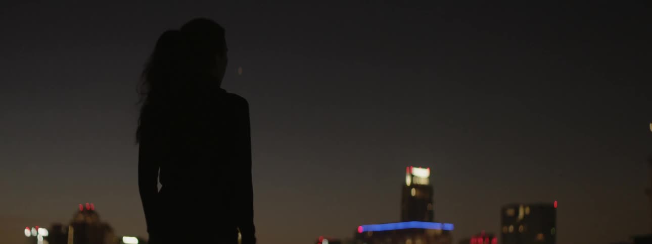 A female athlete is standing outside on a rooftop in the city at night