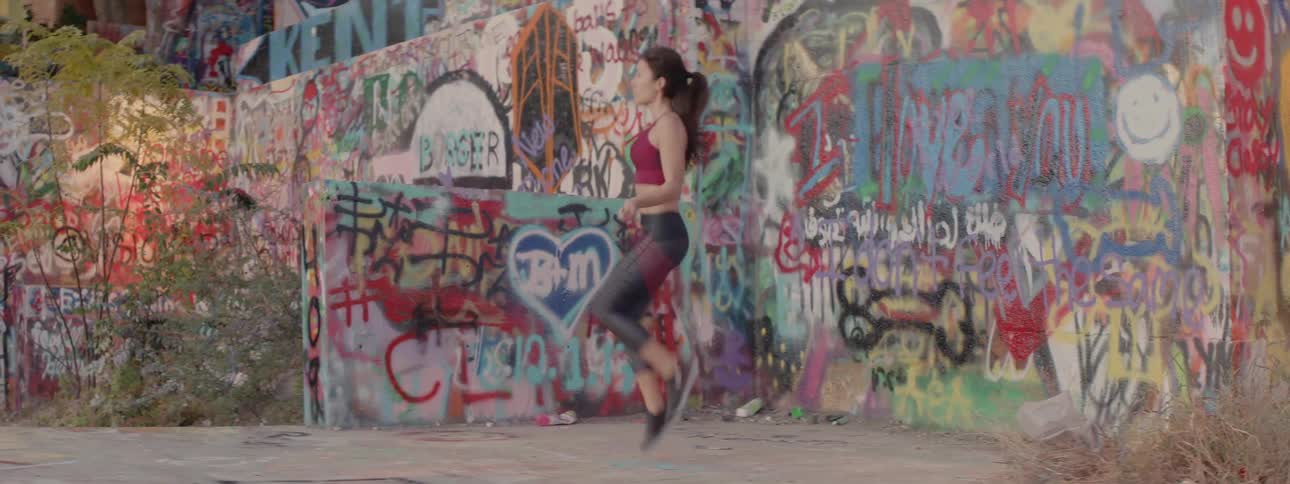 Woman jumping rope rapidly outdoors in a city next to a wall covered with graffiti