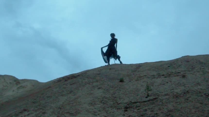 A woman wearing a dress is walking along a ridge line at dusk in the desert