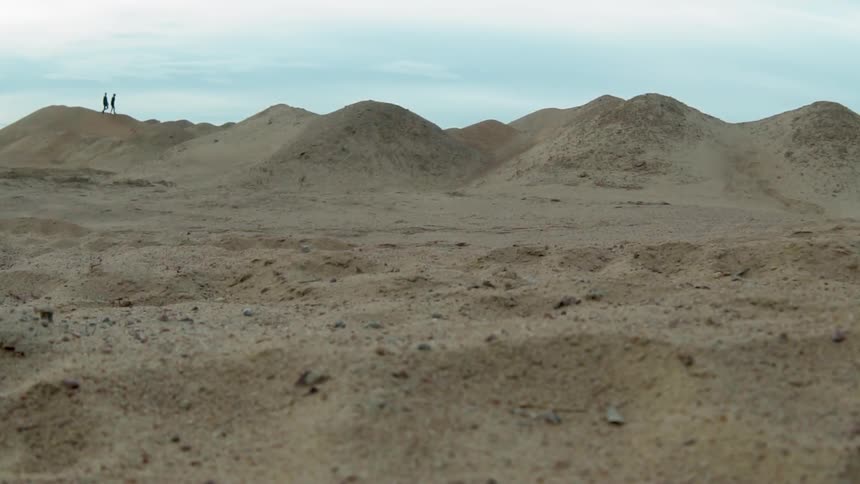 Two people walk on sandy hilly land