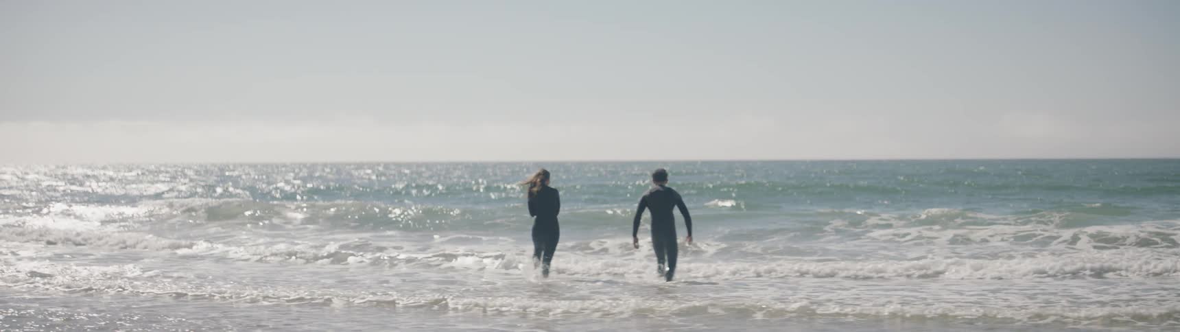 A man and woman in wet suits wad into the ocean