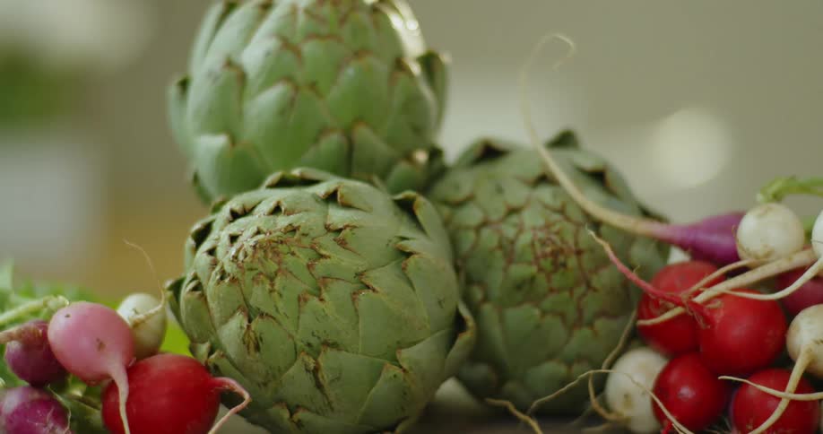 Artichokes and radishes sit on a cutting board
