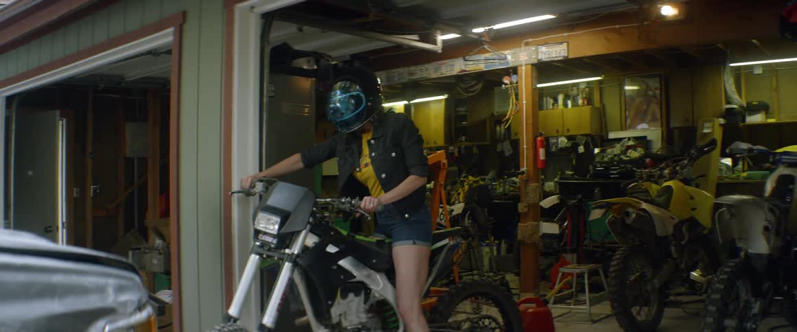 A girl is getting on a motorcycle inside a garage