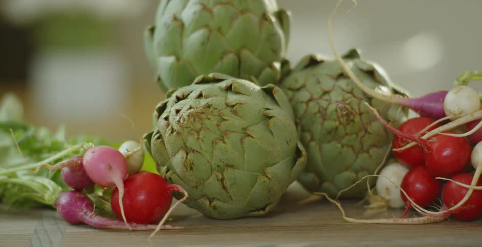 Artichokes and radishes sit on a cutting board