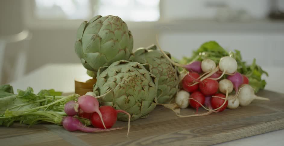 Artichokes and radishes sit on a cutting board