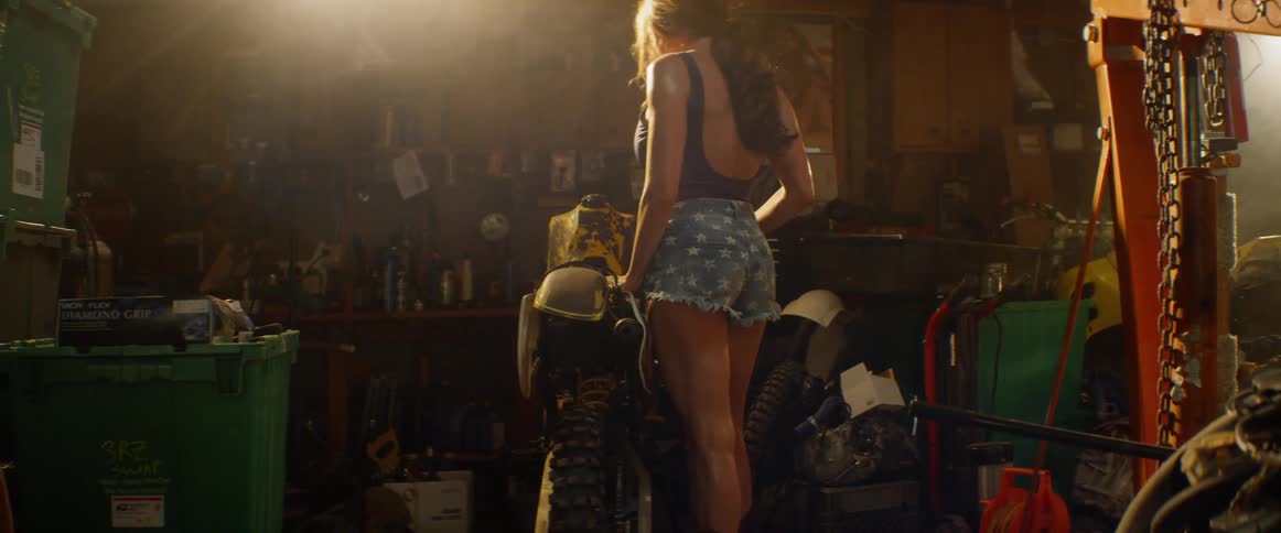 A woman stands next to a motorcycle in a garage with a power tool
