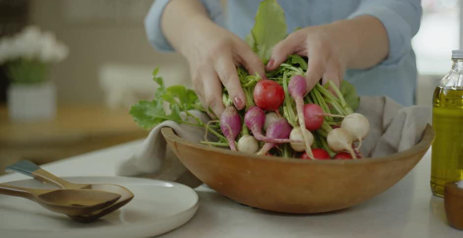A woman puts a bunch of radishes into a wooden bowl