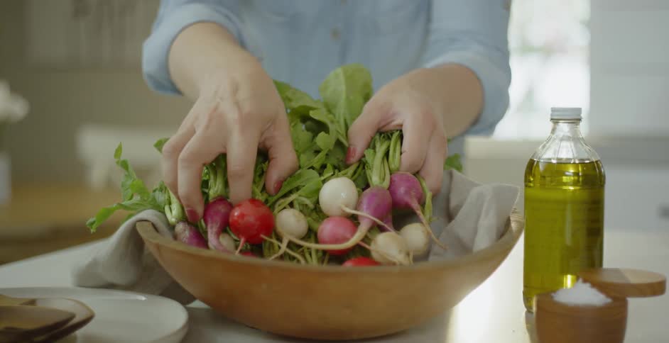 Person arranges a bunch of radishes in a brown bowl