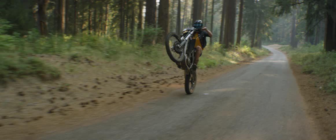 A woman is doing a wheelie as she rides a motorcycle in a natural setting during the day