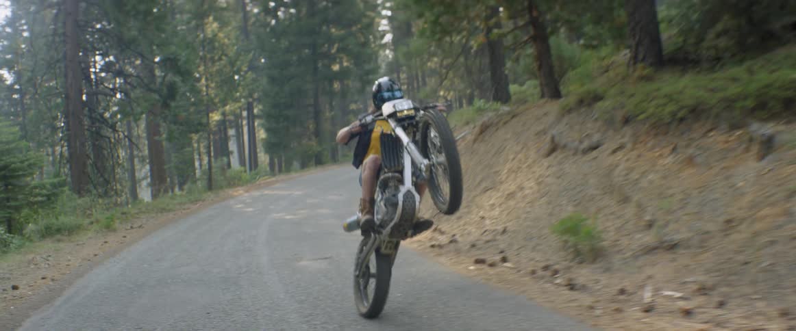A woman is doing a wheelie as she rides a motorcycle in a natural setting during the day