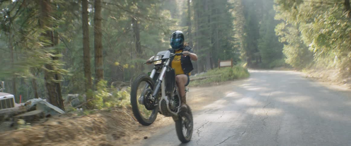 A woman pops a wheelie on a motorcycle on a dirt road