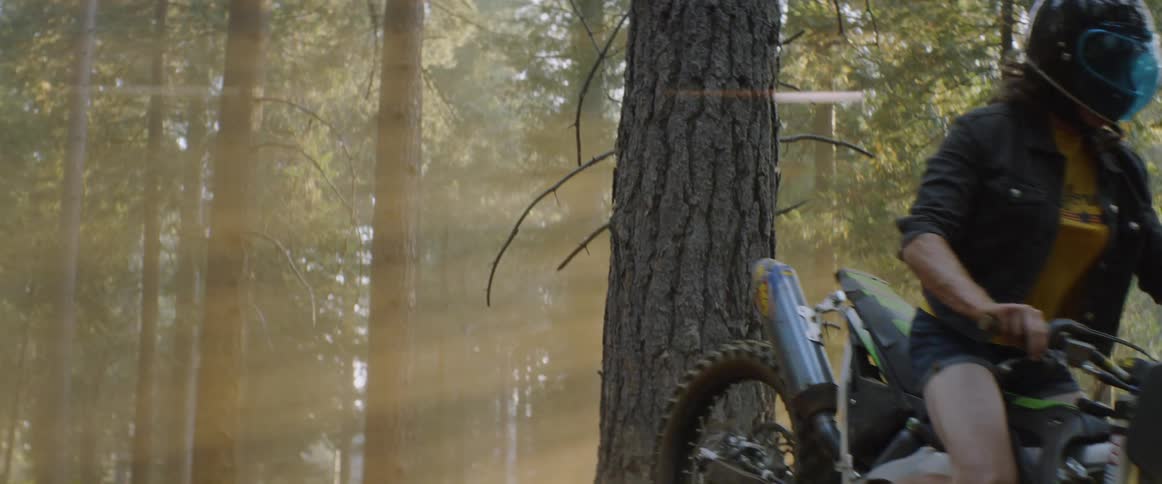 Woman wearing a helmet drives a motorcycle through the woods