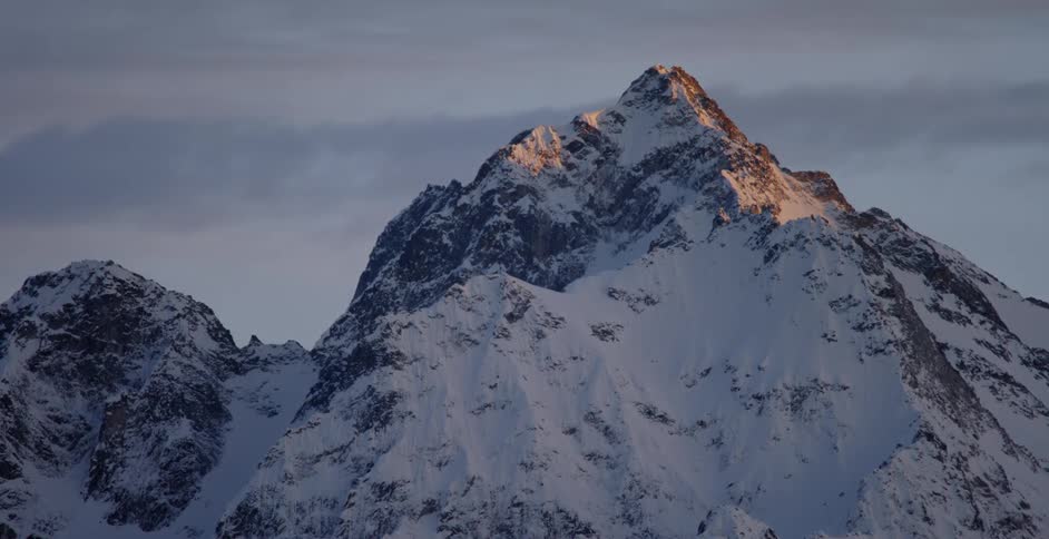 Clouds float over a snowy mountain peak at sunset