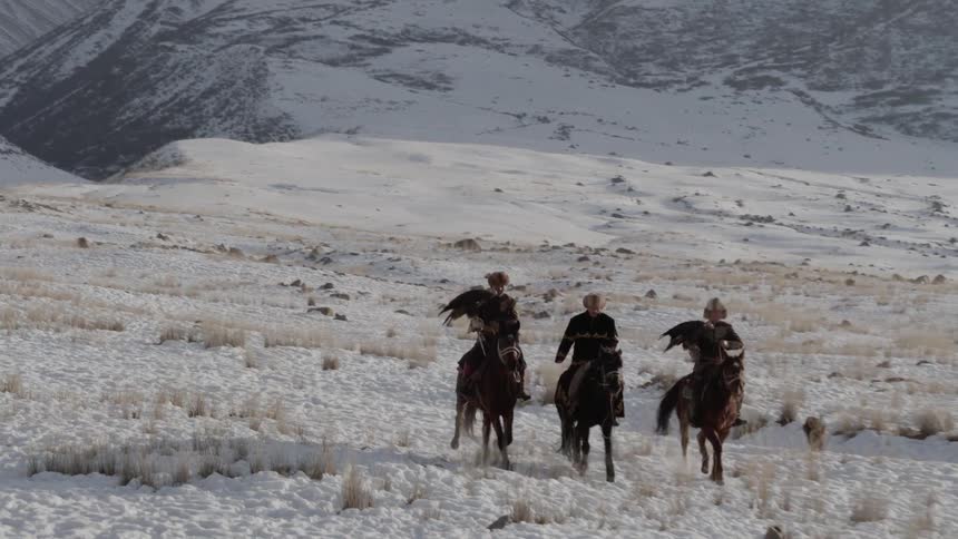 People ride horses across a snowy landscape