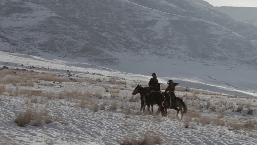 Three people ride horses on the snow covered hills