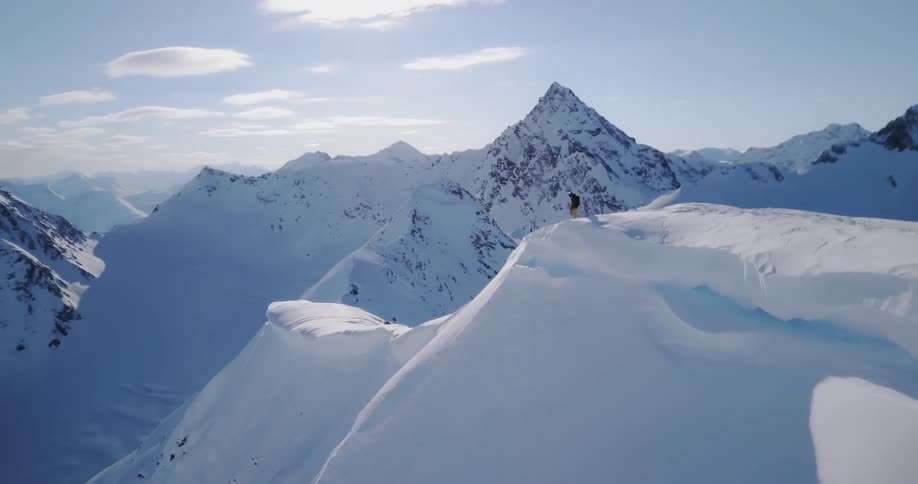A man stands on top of a snowy mountain top