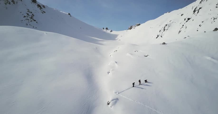 People are hiking up a mountain covered in snow on a sunny day