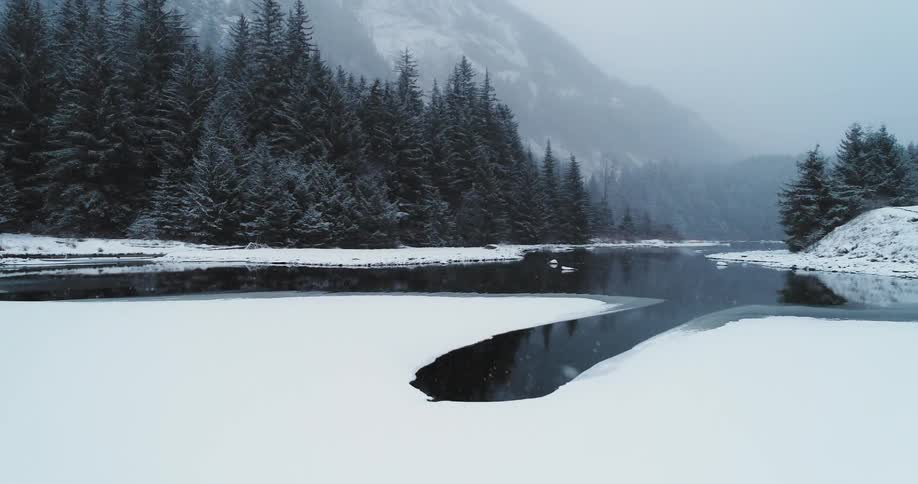 Snow flurries are falling over a river running through a natural setting