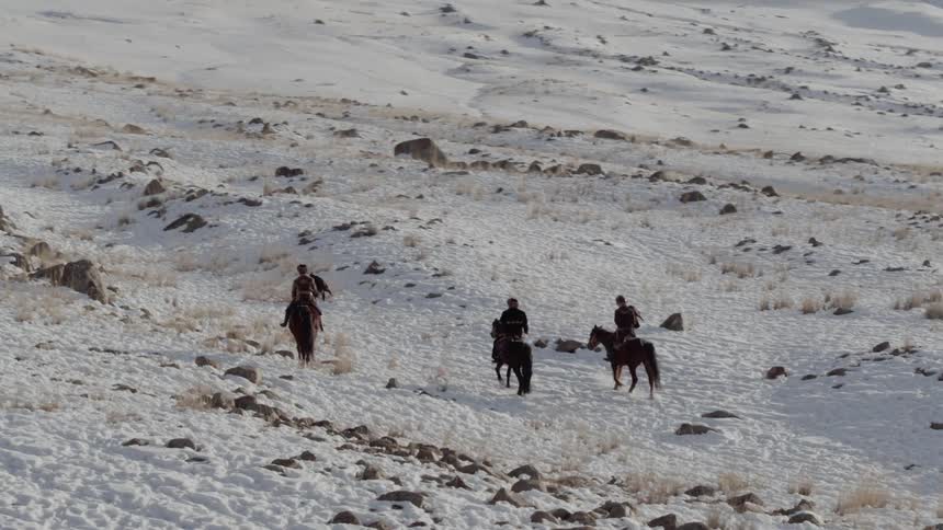 Three people ride horses on the snow covered hills
