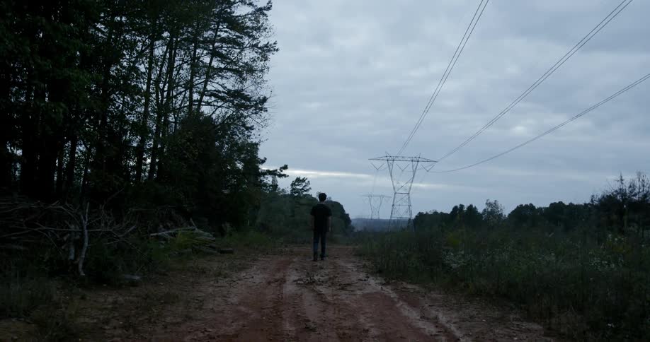 A young man walks down a dirt trail
