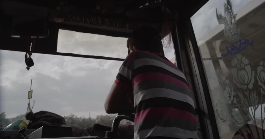A man is leaning on a handrail as he rides in a bus during the day