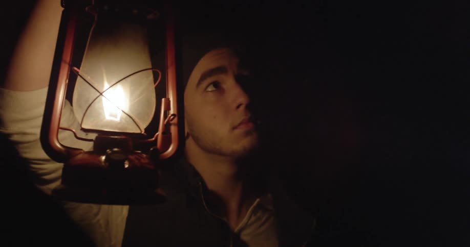 A man holds a flame lantern in the dark