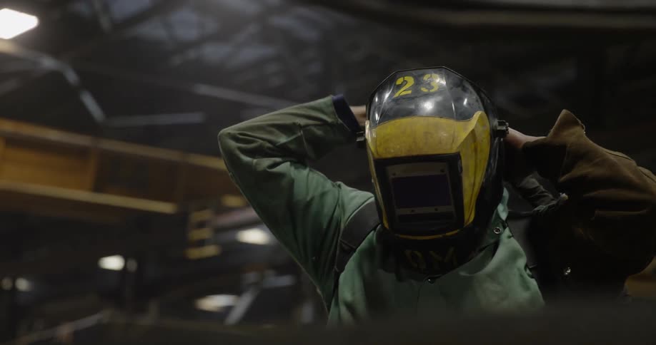 A welder affixes his welding mask inside the warehouse