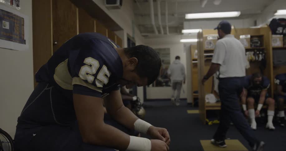 Football player sits on bench in locker room