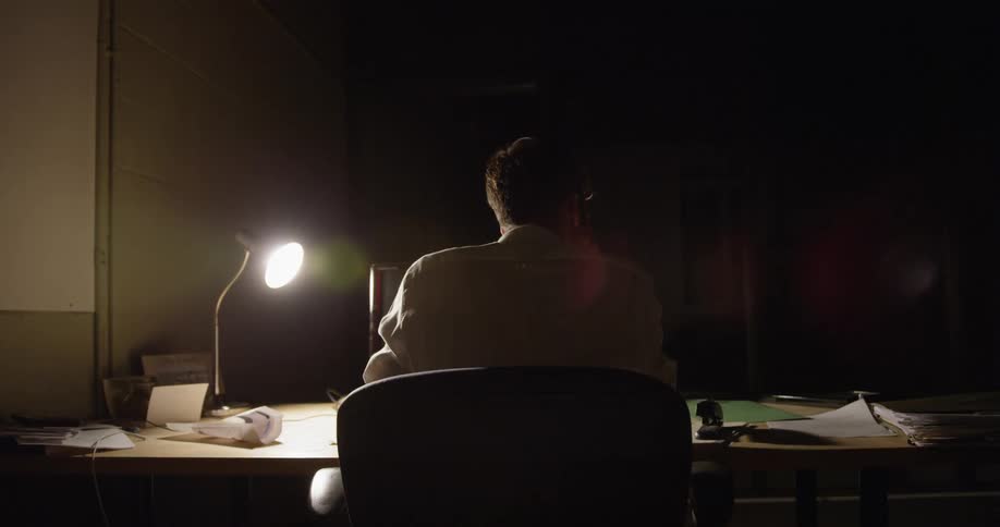 A man sits at a desk in a dark room