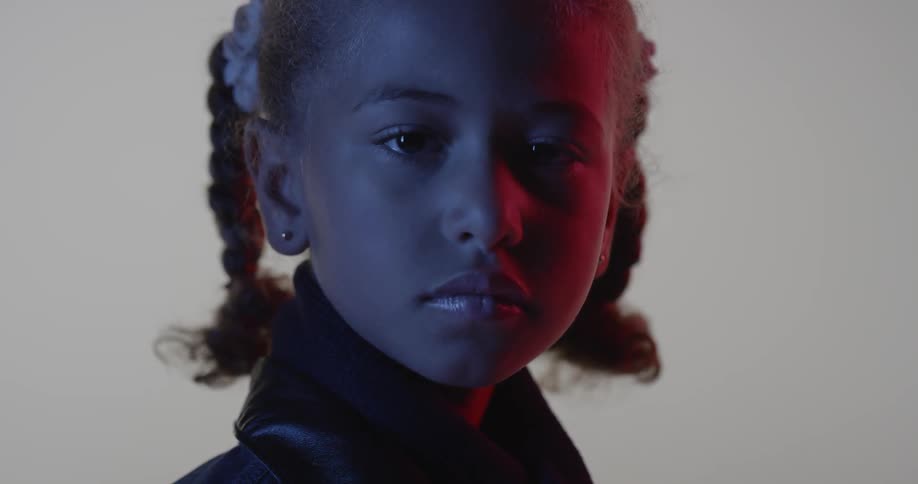 A young girl stares blankly in a dim room