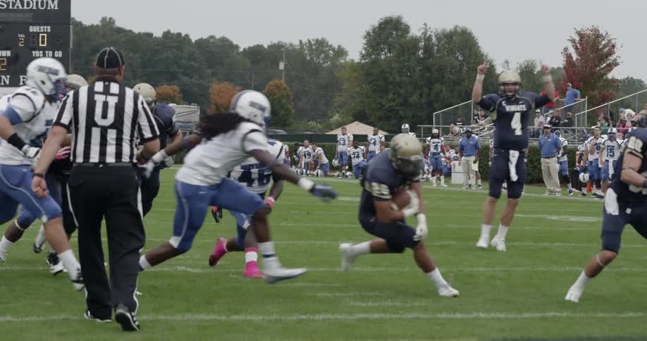 The football players are running on the field, one has the ball