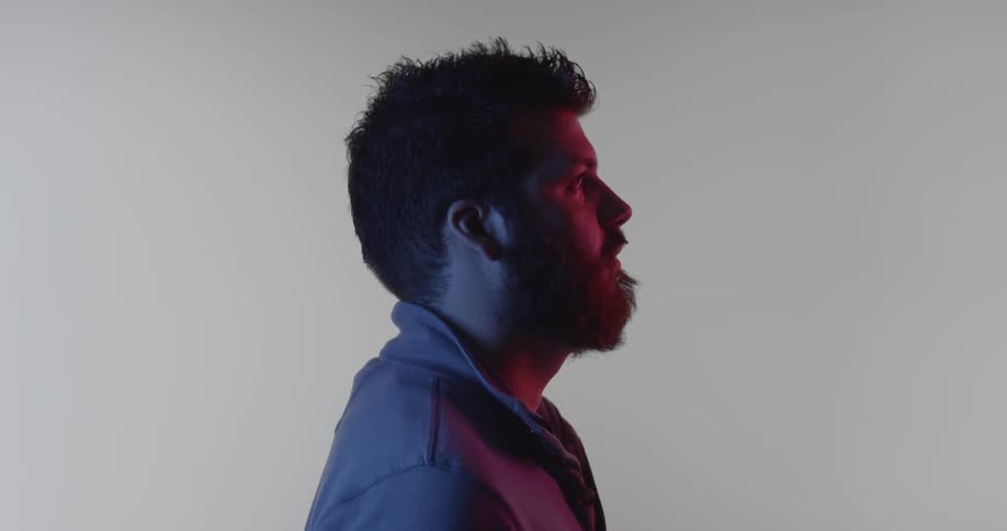 A man is lit with purple and pink lights against a white background