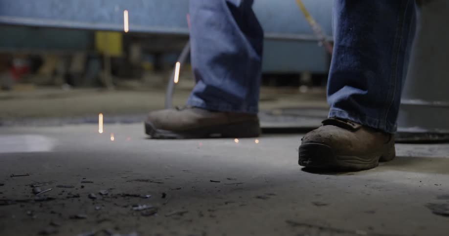 A person is working in a shop with sparks falling to the ground
