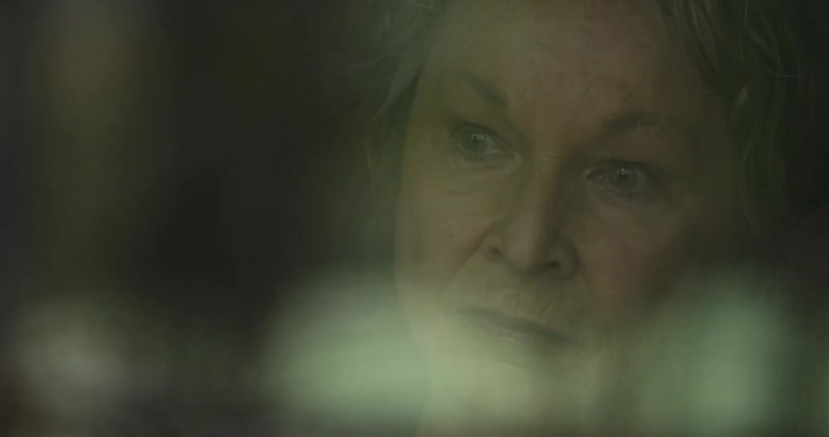 An older woman is watching the rain fall outside of her window