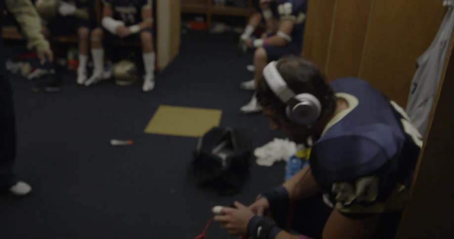 A football player wears headphones in a locker room