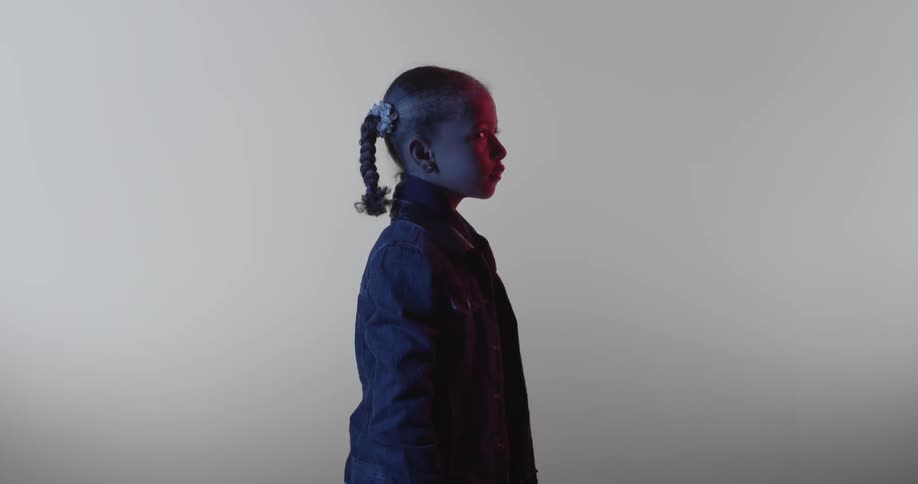 A young girl stares blankly in a dim room