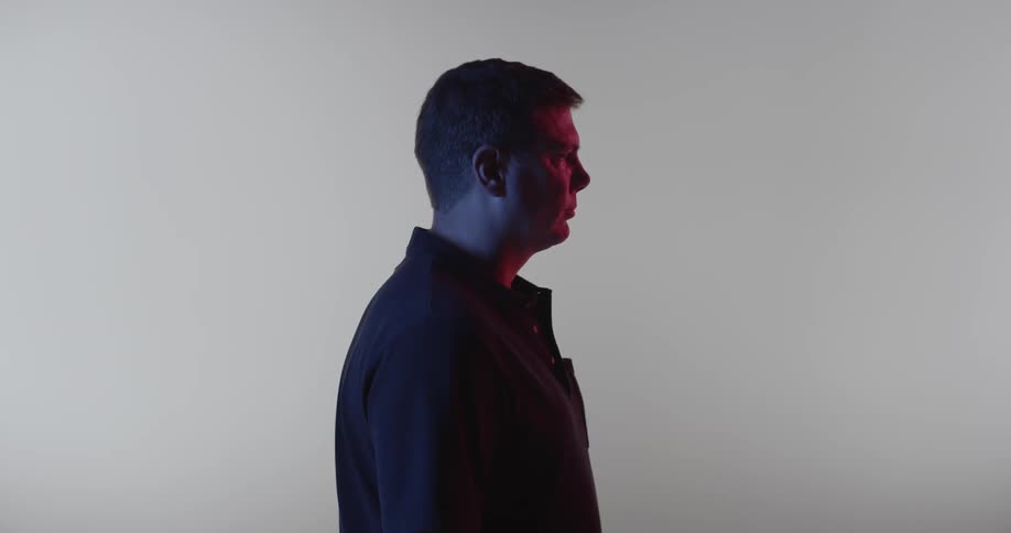 A man with purple and pink light on him is facing is left