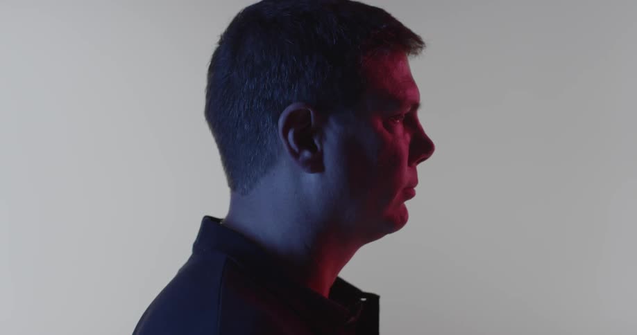 A man stares forward inside a room with a white backdrop