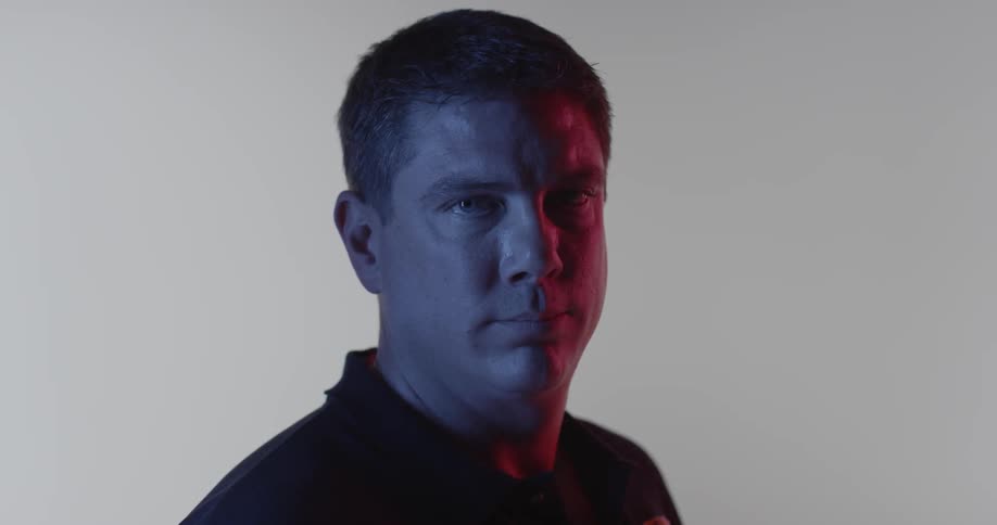 A man stares forward inside a room with a white backdrop