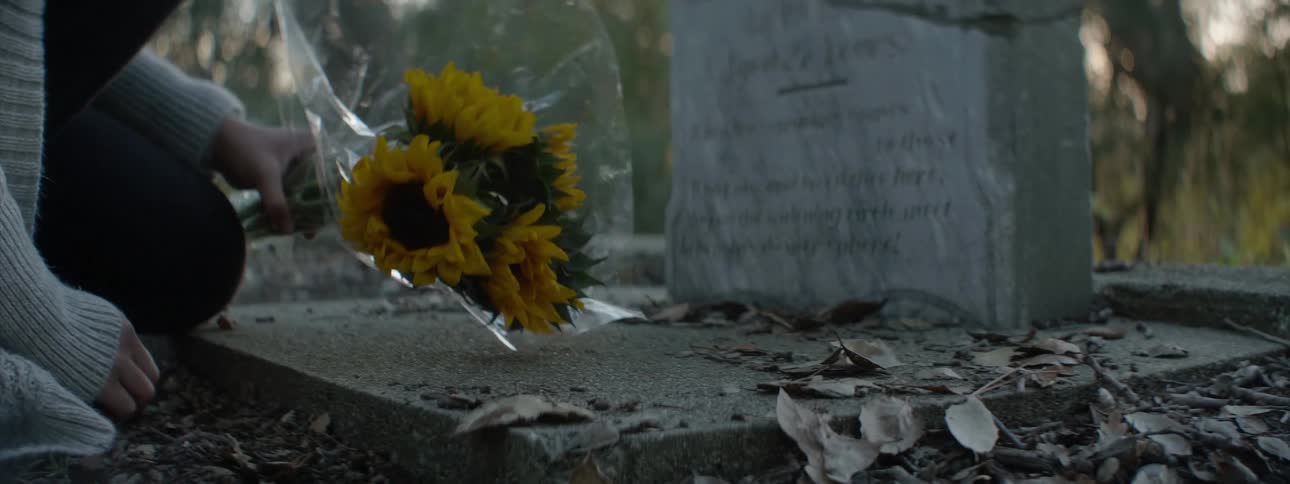 A woman places flowers in front of a headstone
