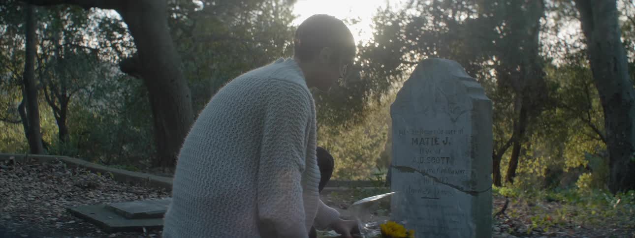 Woman crouched and placing flowers before a headstone at sunset