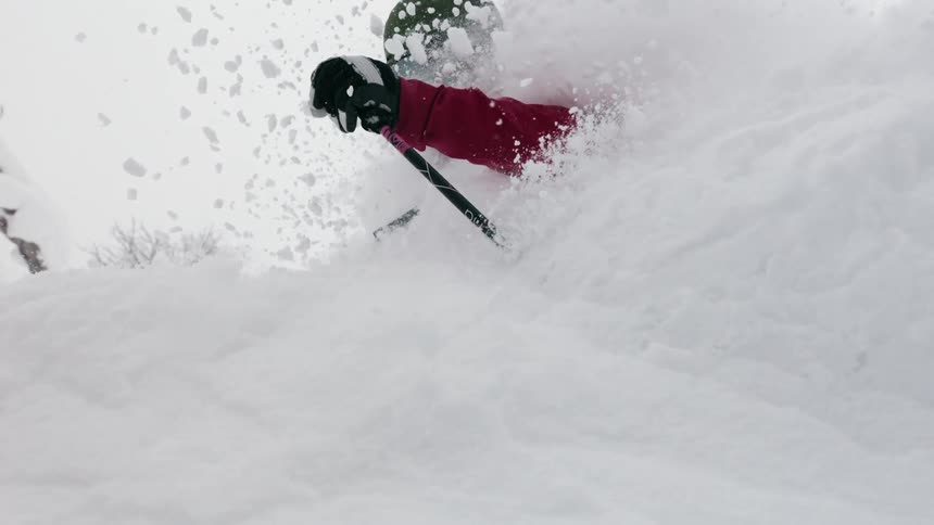 Skier kicking up deep snow as she passes by down a slope