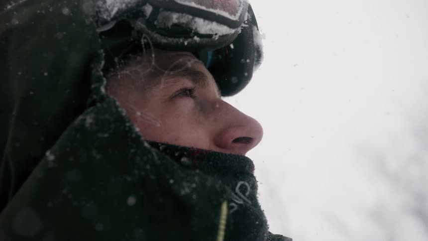 A warmly dressed man watches it snow outside