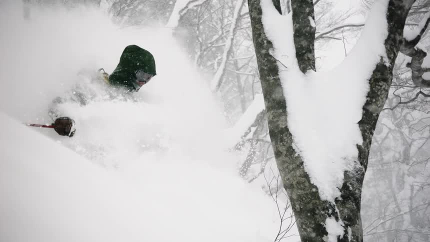 Skier going down a hill in deep snow as it flies all around