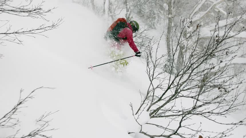 A skier is turning through deep snow as she goes down a hillside in daylight