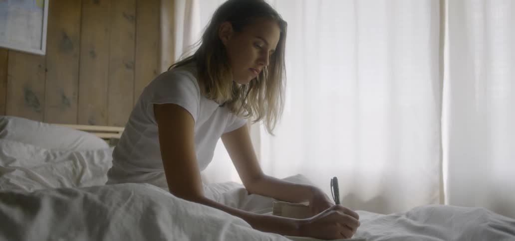 A woman sits in bed and writes in a notebook